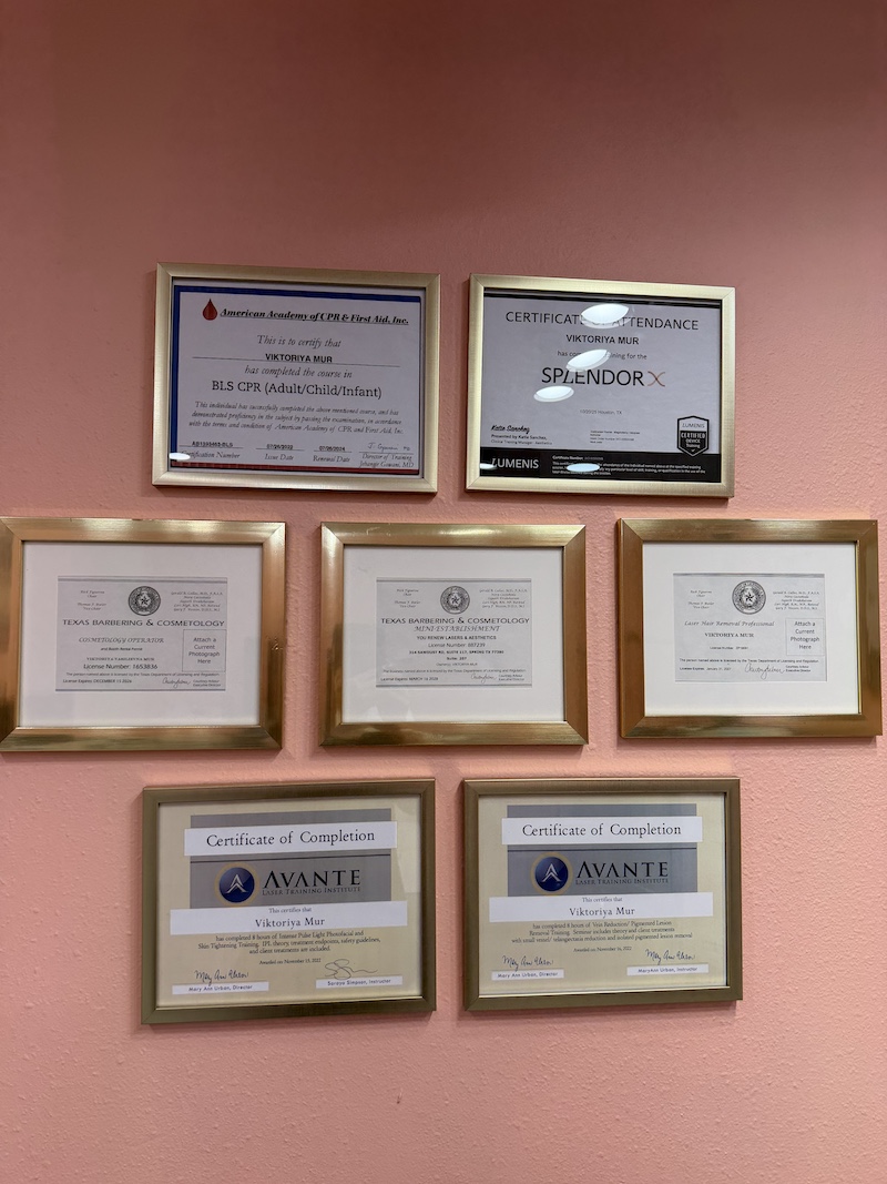 Wall featuring eight framed certificates on a peach-colored wall, arranged in two rows (top row two frames, bottom row six). The frames display professional licenses and completion certificates from organizations like Avante and Texas Barbering & Cosmetology.
