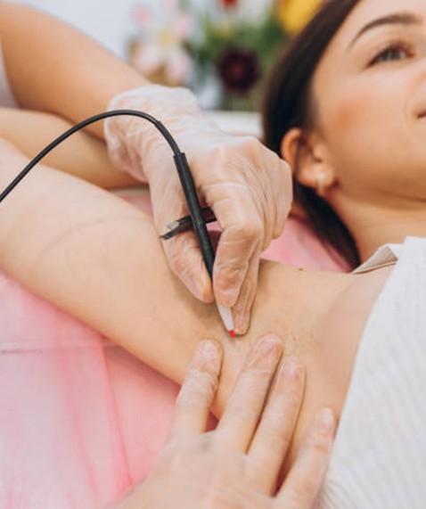 Medical professional in gloves performing a diagnostic ultrasound or probe-based exam on a patient lying down, device pressed to the underarm with a cable attached.